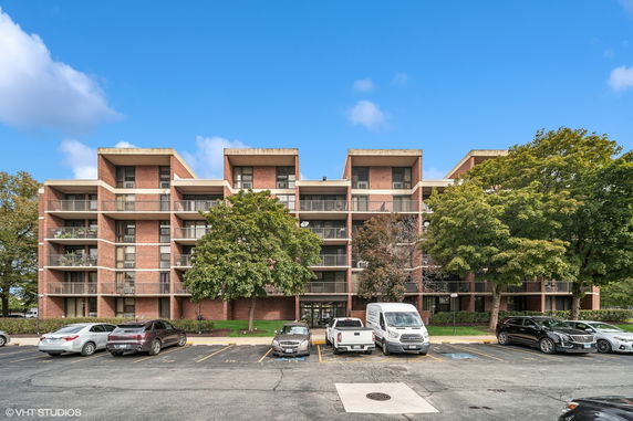 Front view of a multi-story apartment building with balconies and parking area.
