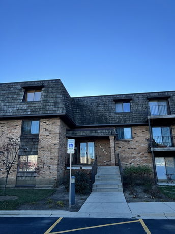 Front view of a two-story brick building with a shingled roof and a staircase leading to the entry.