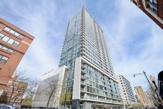 Front view of a tall modern residential building with glass balconies and multiple floors.