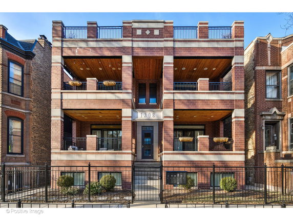 Front view of a multi-story brick residential building with balconies and a central entrance.
