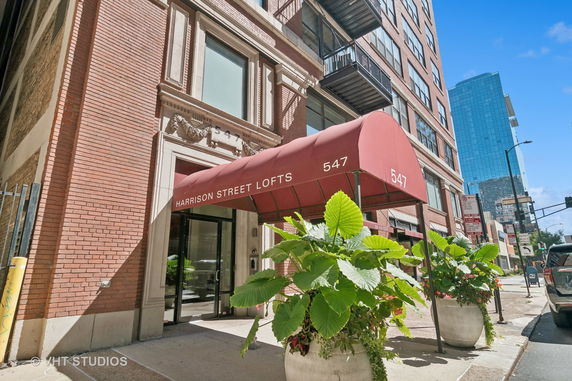 Front view of a multi-story building with a red awning labeled 'Harrison Street Lofts' and street entrance.