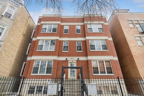 Front view of a three-story brick building with multiple windows and a gated entrance.