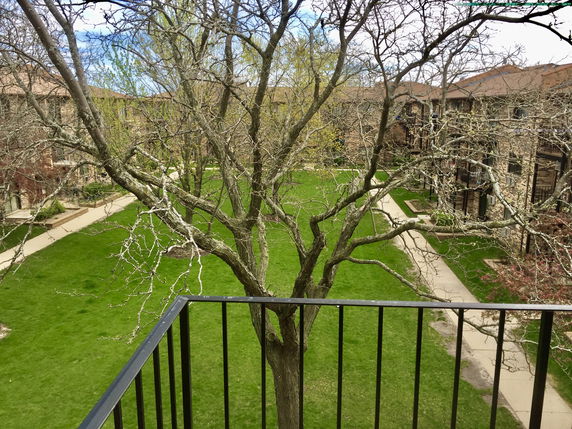Panoramic view from a balcony overlooking a grassy courtyard surrounded by multi-story buildings.