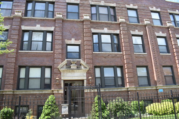 Front view of a multi-story brick building with several windows and a gated entrance.