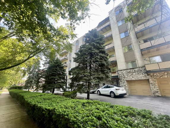 Front view of a multi-story apartment building with balconies and garage entrances on the ground floor.