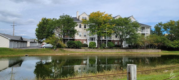 View of a building complex with trees and a pond in the foreground.