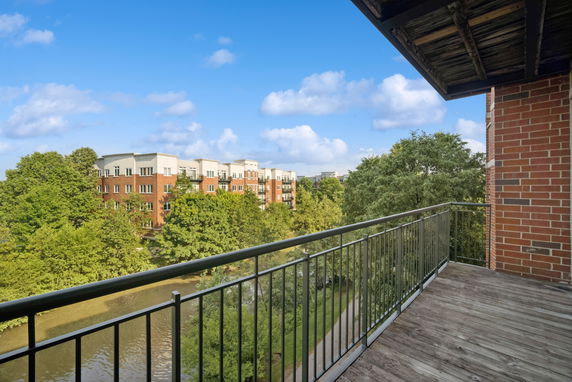 View from a balcony overlooking trees, a water body, and a multi-story brick building.