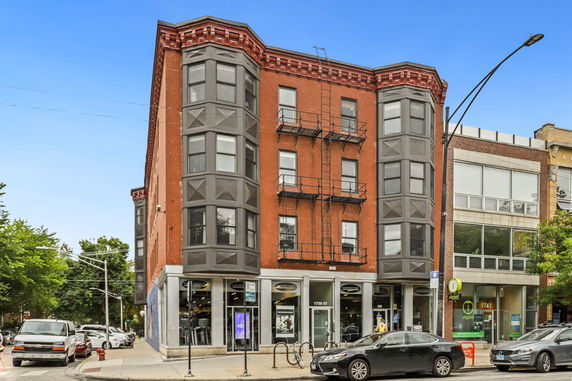 Front view of a multi-story brick building with large windows and a retail space on the ground floor.