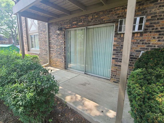 Exterior view of a brick building with a sliding glass door and a concrete patio.
