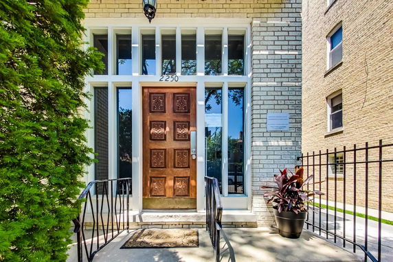 Front view of a brick building entrance with a decorative wooden door and large windows.