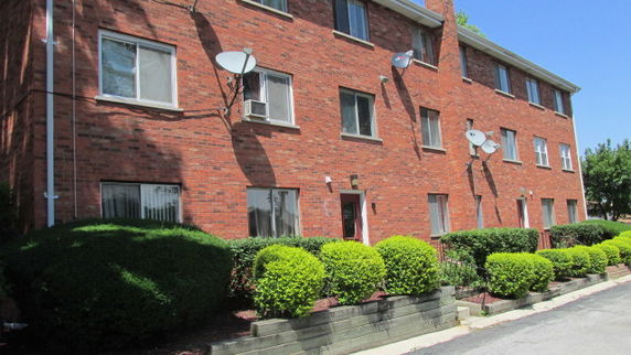 Front view of a three-story brick apartment building with multiple satellite dishes.