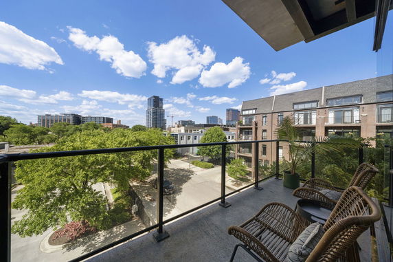 View of the surrounding buildings and trees from a balcony with wicker chairs.