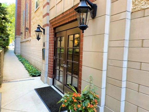 Entrance view of a building with brick and beige siding, featuring glass door and decorative lanterns.