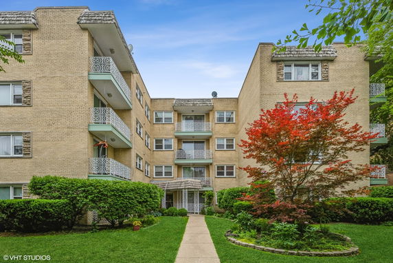 Front view of a multi-story apartment building with decorative balconies and a landscaped garden.