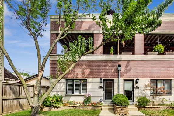 Front view of a two-story house with a brick facade and a wooden pergola on the second floor.
