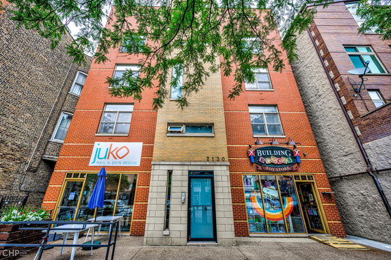 Front view of a three-story building with brick facade and ground floor retail spaces.