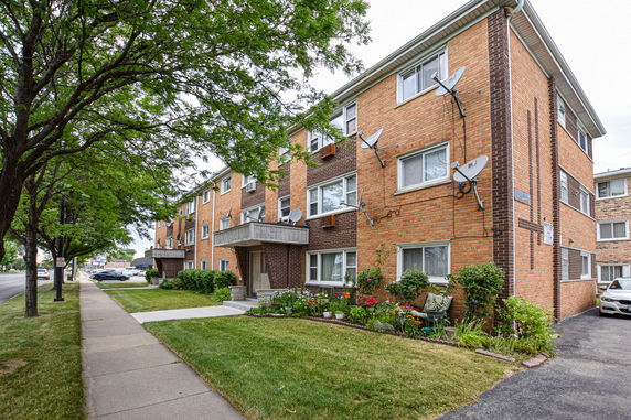 Front view of a three-story brick apartment building with satellite dishes.
