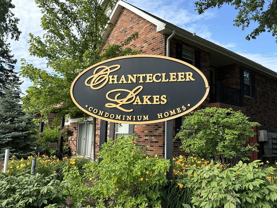 Front view of a brick condominium building with a sign reading 'Chantecleer Lakes Condominium Homes.'