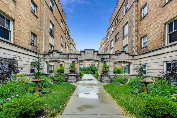 Front view of a multi-story brick building with an ornate stone archway and landscaped pathway.