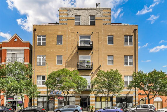 Front view of a multi-story building with balconies and storefronts on the ground level.