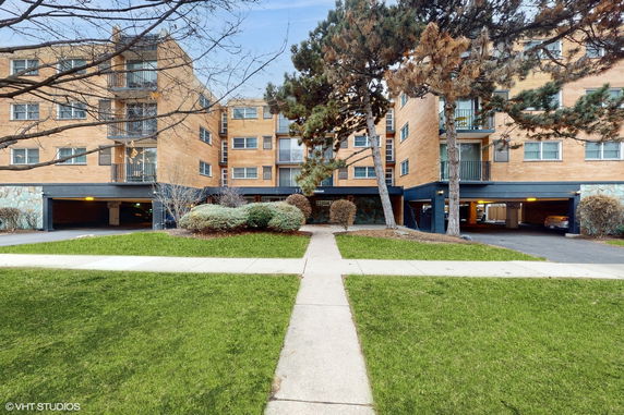 Front view of a multi-story residential building with balconies and parking beneath.