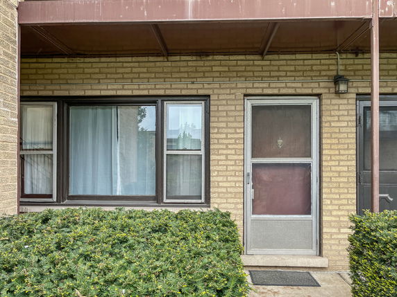 Front view of a brick house entrance with a screen door and large window.