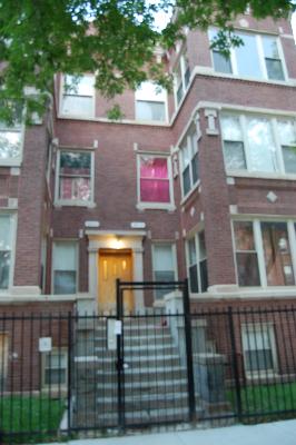 Front view of a multi-story brick building with a gated entrance and steps.