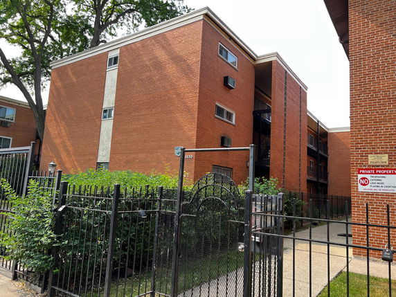 Front view of a multi-story brick apartment building with gated entrance.
