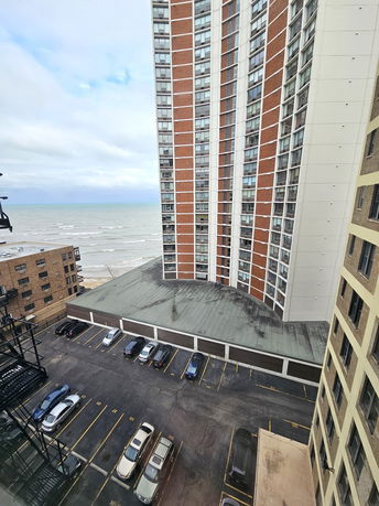 View from high-rise building showing other buildings, a parking area, and a body of water in the background.