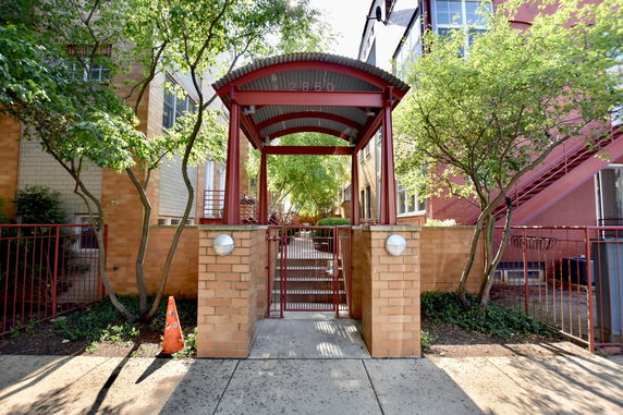 Front view of a gated residential building entrance with a red metal arch.
