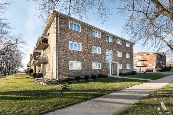 Front view of a three-story brick apartment building with balconies.