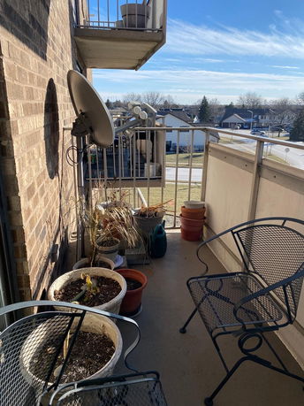 Balcony view with outdoor chairs, potted plants, and a satellite dish overlooking a residential area.