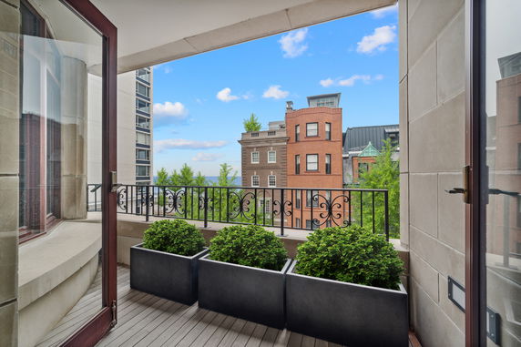 View from a balcony with potted plants and railings, overlooking buildings.