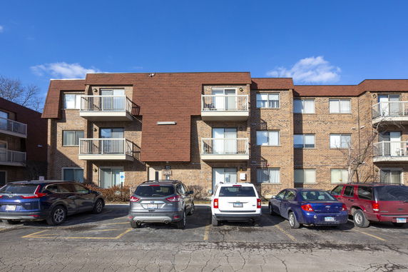 Front view of a three-story apartment building with balconies and parking area.