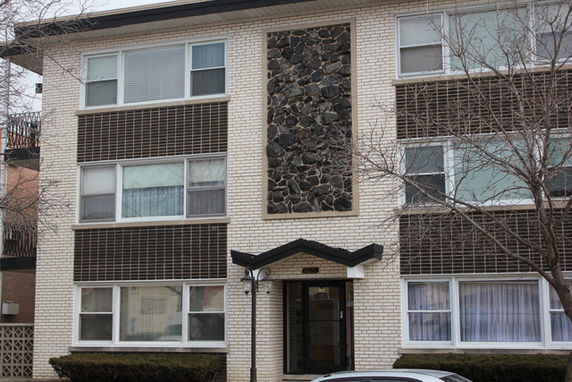 Front view of a three-story brick apartment building with stone paneling.
