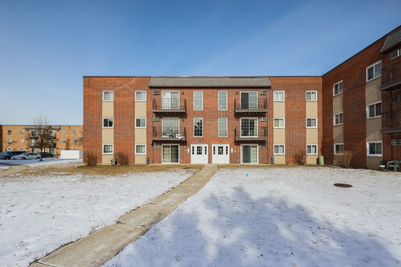 Front view of a three-story brick apartment building with balconies.