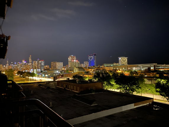 Nighttime panoramic view of a city skyline with buildings illuminated, featuring heart-shaped lights on two prominent buildings.
