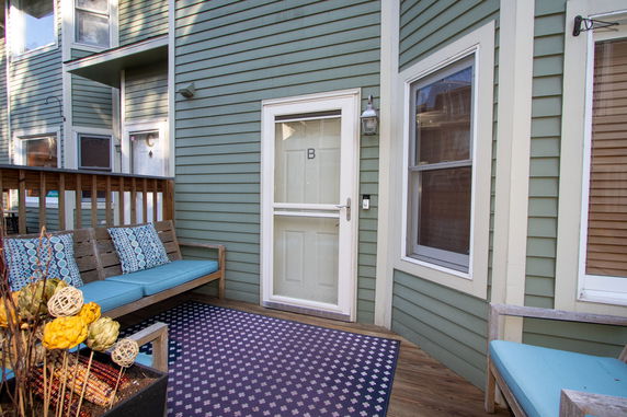 Front view of a building entrance with a wooden bench and outdoor rug.