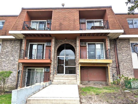 Front view of a multi-story brick apartment building with balconies and a central entrance.