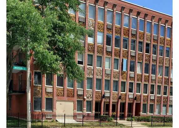 Front view of a multi-story brick building with ornate decorative panels and numerous windows.