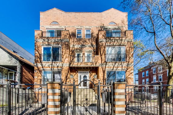 Front view of a multi-story brick building with balconies and a gated entrance.
