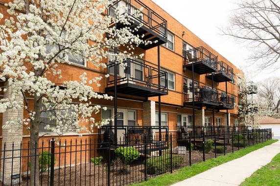 Front view of a three-story apartment building with balconies and flowering trees.