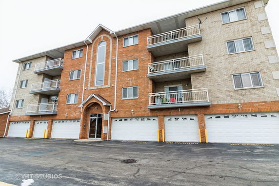 Front view of a multi-story apartment building with balconies and garages.