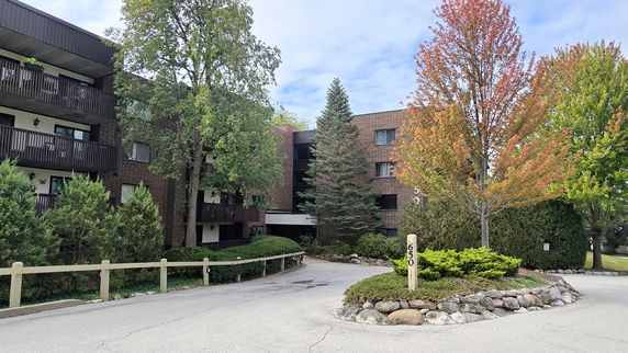 Front view of a multi-story brick apartment building with balconies and surrounding trees.