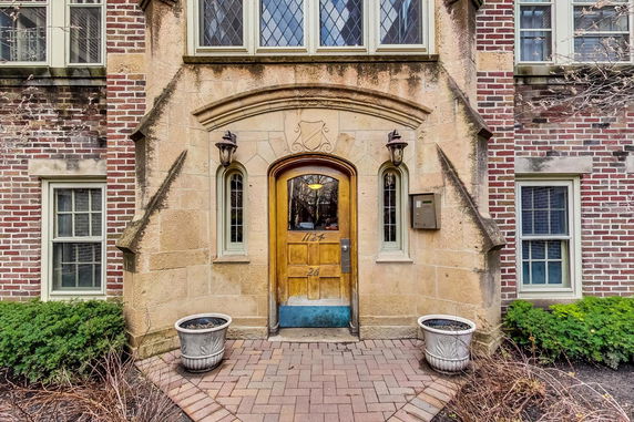 Front view of a building entrance with stone and brick facade, wooden door, and decorative windows.