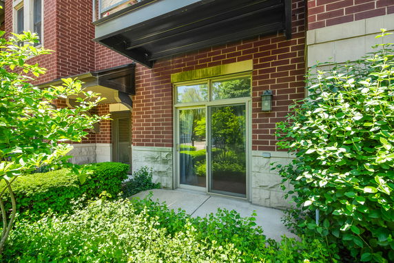 Exterior view of a brick building with a sliding glass door and greenery.