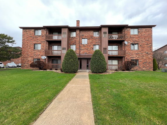 Front view of a three-story brick apartment building with balconies.