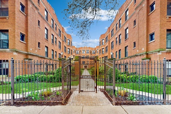 Front view of a multi-story brick building with gated entrance and landscaped walkway.