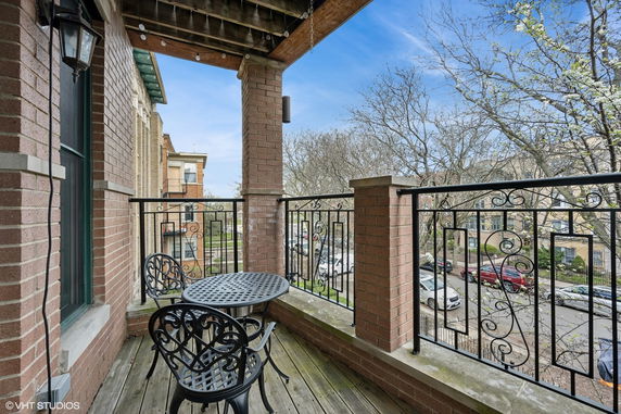 View of surrounding neighborhood from a balcony with metal railings and a small table with chairs.