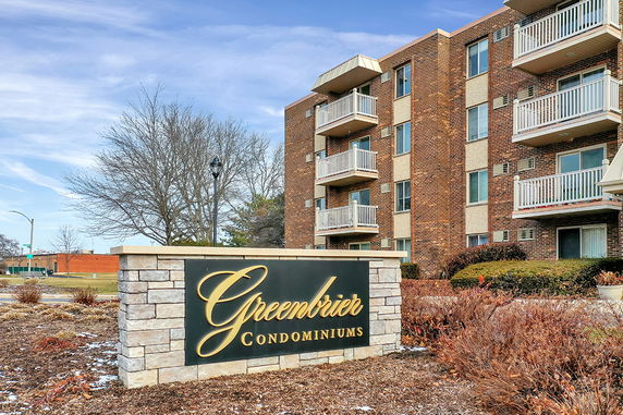 Front view of a multi-story condominium building with balconies and a sign that reads 'Greenbrier Condominiums'.